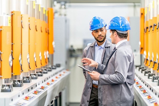 Two men in blue hard hats inside a factory